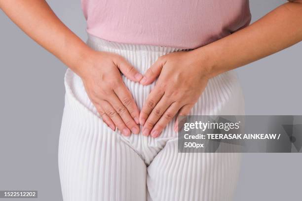 midsection of woman with hands on stomach standing against gray background - órgão reprodutor humano - fotografias e filmes do acervo
