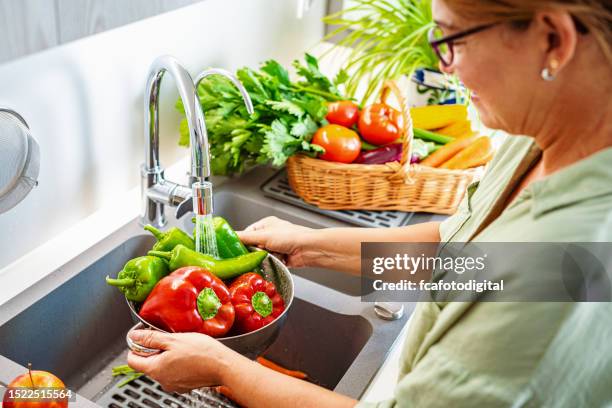 woman washing fresh vegetables in a colander - bell pepper stock pictures, royalty-free photos & images