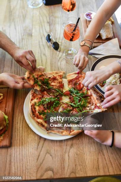 friends tearing pieces off pizza while enjoying dinner in restaurant - beer and food stock pictures, royalty-free photos & images