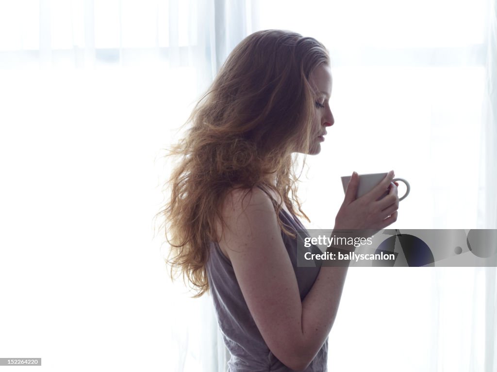 Young Red Haired Woman Looking At Cup In Her Hand.