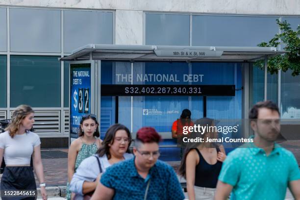 Pedestrians walk past a poster and electronic billboard displayed at 18th and K St's NW that displays the current U.S. National debt per person and...