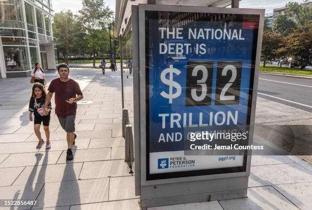 Pedestrians walk past a bus shelter at Pennsylvania Avenue and 22nd Street NW where an electronic billboard and a poster display the current U.S....