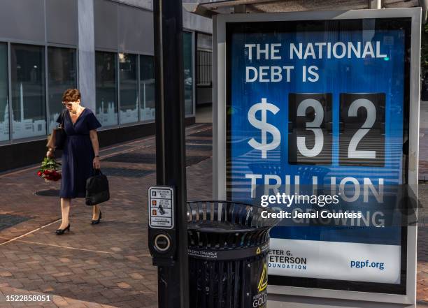 Pedestrians walk past a poster and electronic billboard displayed at 18th and K St's NW that displays the current U.S. National debt per person and...