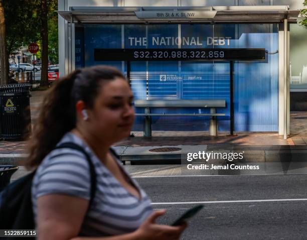 Pedestrians walk past a poster and electronic billboard displayed at 18th and K St's NW that displays the current U.S. National debt per person and...