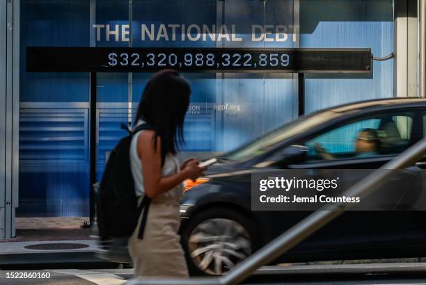 Pedestrians walk past a poster and electronic billboard displayed at 18th and K St's NW that displays the current U.S. National debt per person and...