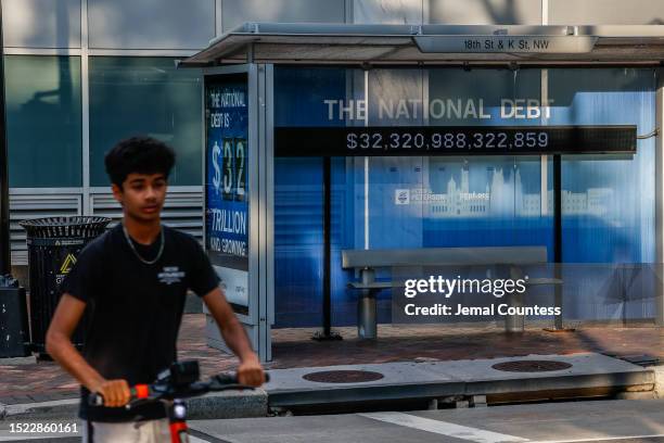 Pedestrians walk past a poster and electronic billboard displayed at 18th and K St's NW that displays the current U.S. National debt per person and...