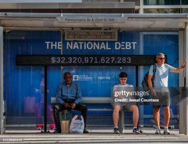 Pedestrians sit at a bus shelter at Pennsylvania Avenue and 22nd Street NW where an electronic billboard and a poster display the current U.S....