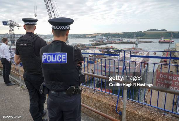 Two policeman watch as the Bibby Stockholm accommodation barge is moved out of dry dock in Falmouth Docks to another location prior to departure to...