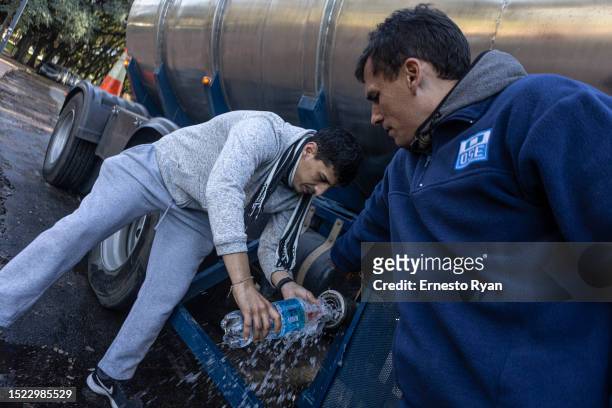Passerby fills a battle from a OSE tank truck with underground water as tap tap water contains high salinity and chemicals on July 07, 2023 in...