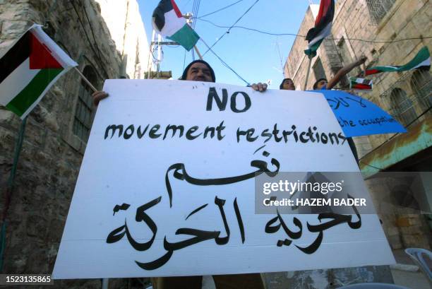 Palestian holds up a sign in English and Arabic that reads, " No movement restriction, yes to freedom of movement", during a rally along Shuhada...