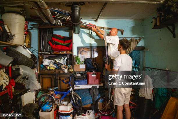 caucasian father and teenage boy decluttering sport equipment, from the messy garage - declutter stockfoto's en -beelden