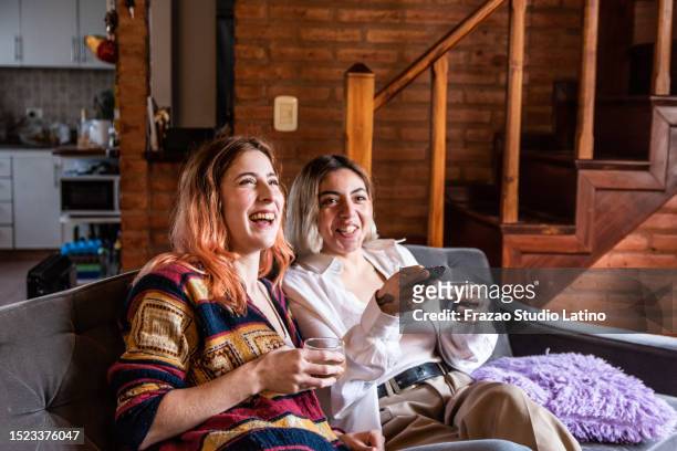 jeune couple de lesbiennes regardant la télévision / film assis sur un canapé dans le salon - movie film reel photos et images de collection