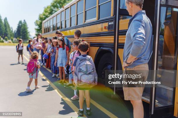 elementary age students waiting to board school bus - viagem-de-estudo imagens e fotografias de stock