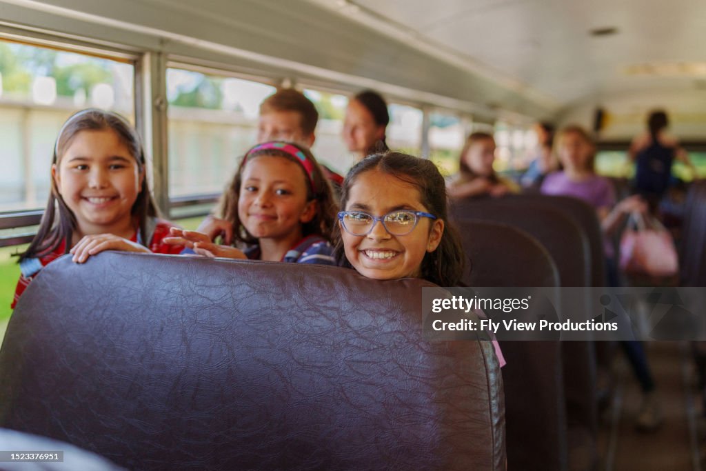 Glückliche Freundinnen im Grundschulalter, die zusammen Schulbus fahren