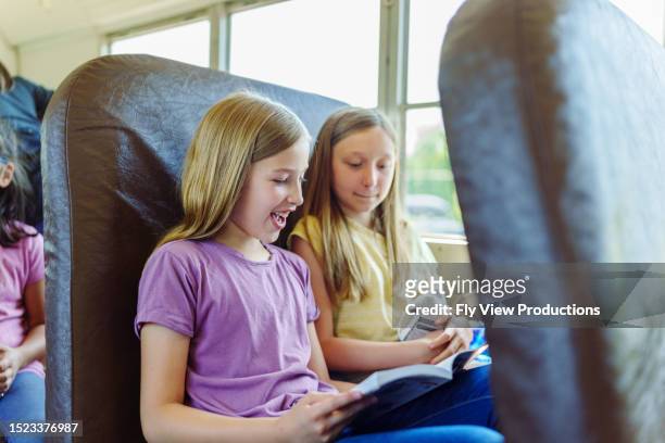amici che guardano un libro insieme mentre viaggiano sullo scuolabus - young girl reading book bus foto e immagini stock