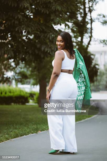 graceful black woman in white suit with green jacket exploring park finding inspiration in beauty of nature - curvy model stock pictures, royalty-free photos & images