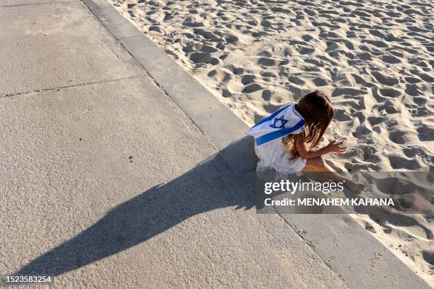 Girl sits with an Israeli flag by the sand along a beach during a protest against the Israeli government's judicial overhaul bill outside the US...