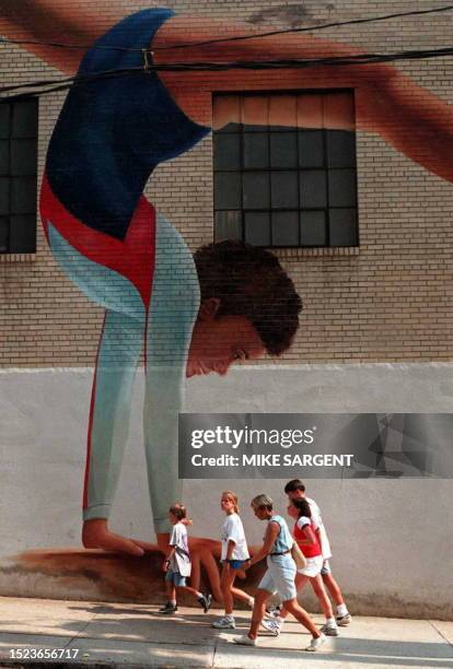 Pedestrians walk past a mural of an Olympic gymnast in painted on a building in downtown Atlanta, GA 02 July. Crowds are beginning to arrive in the...