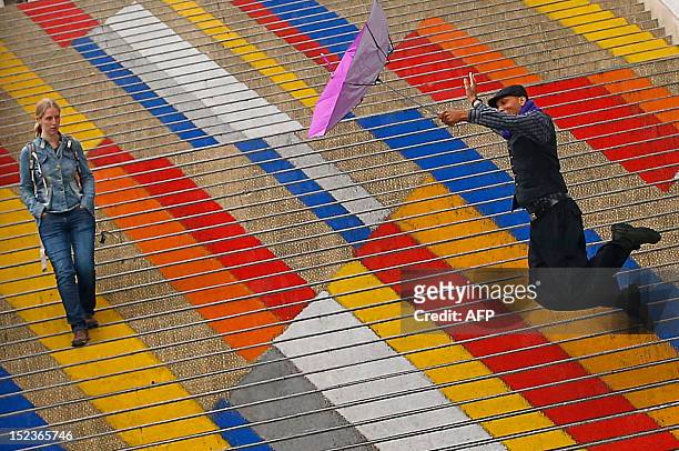 Canadian tourist holds an umbrella as he jumps on the colored steps of the Albertina museum during a rainy day in Vienna on September 19, 2012. AFP...