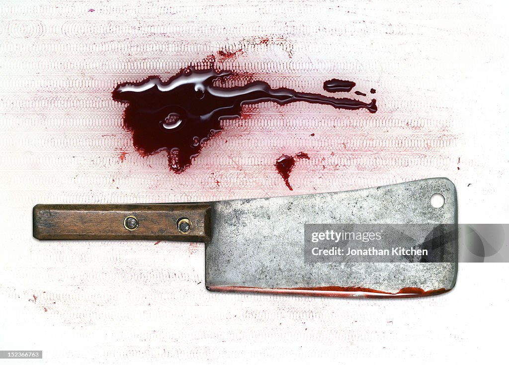 A meat cleaver and blood on a chopping board