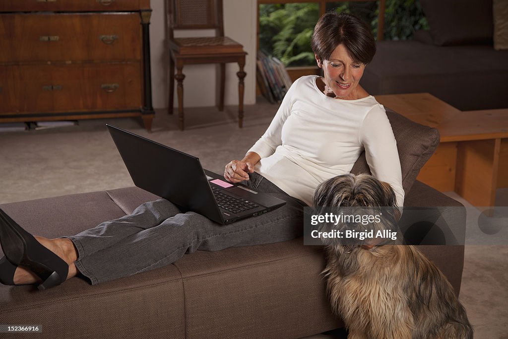 Senior woman using laptop, dog sitting beside