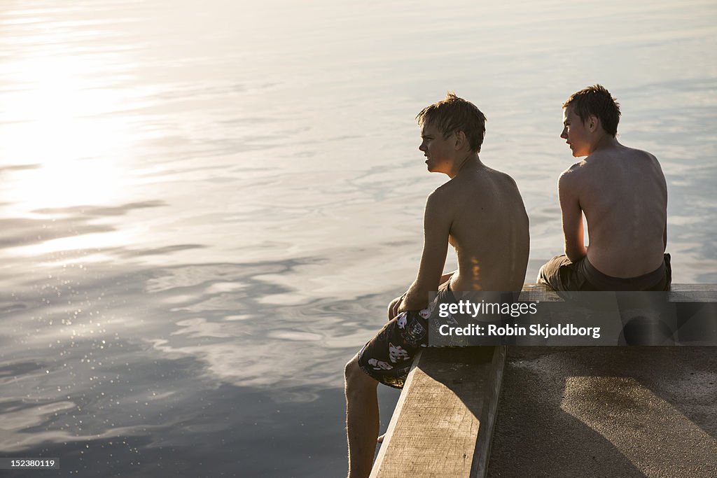 Boys in swimming trunks sitting on pier