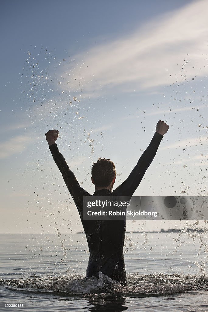 Man in wetsuit with arms in the air, splashing