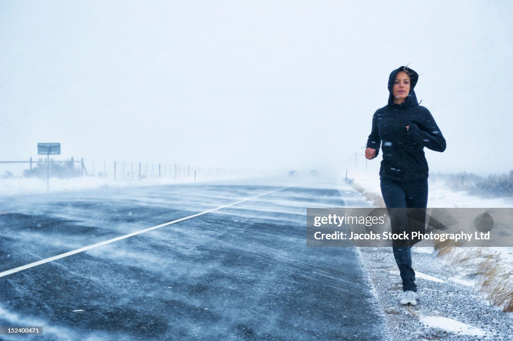 Hispanic woman jogging on snow covered road