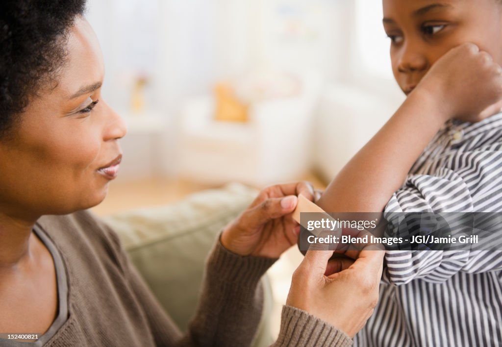 Black mother putting bandage on son's elbow