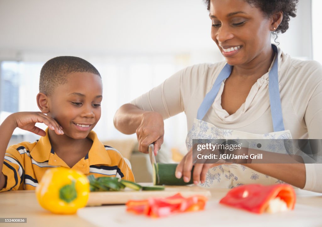 Black son watching mother slicing vegetables