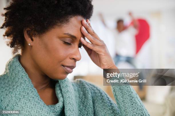 black woman with headache and playful son in background - mom head in hands stock pictures, royalty-free photos & images
