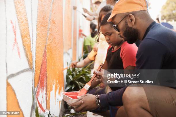 people painting wall together - zusammenhalt stock-fotos und bilder