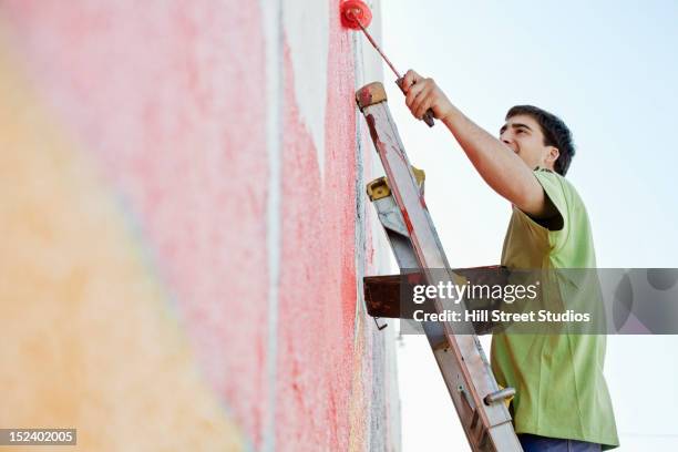 mixed race man painting wall - wandmalerei stock-fotos und bilder