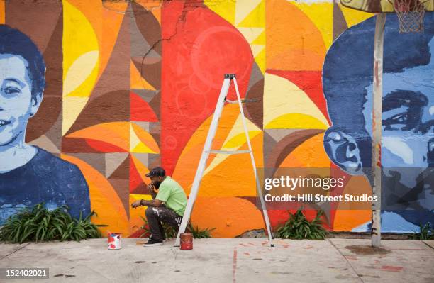 black man sitting on ladder by mural - murale foto e immagini stock