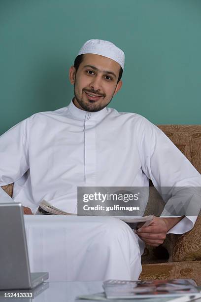 young man sitting in the sofa, holding newspaper - dish dash stock pictures, royalty-free photos & images