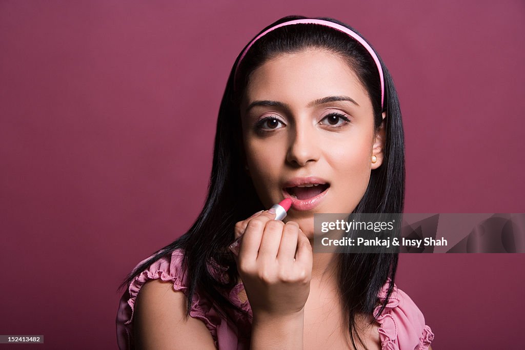 Young woman applying lipstick, portrait