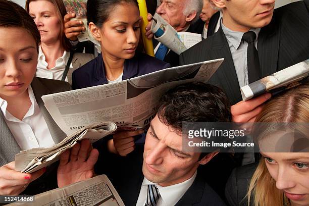 businesspeople reading newspapers on crowded train - beengt stock-fotos und bilder