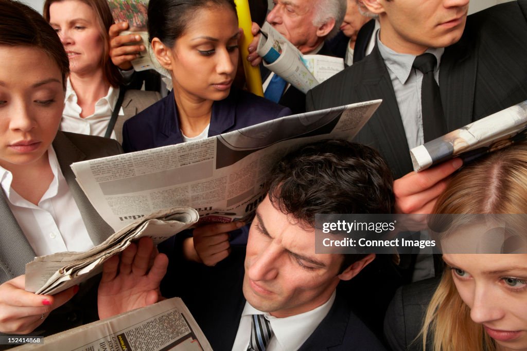 Businesspeople reading newspapers on crowded train