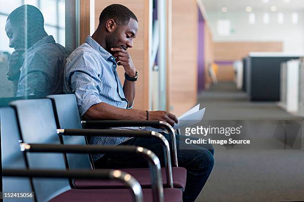 man sitting on chair reading document - colloquio di lavoro foto e immagini stock