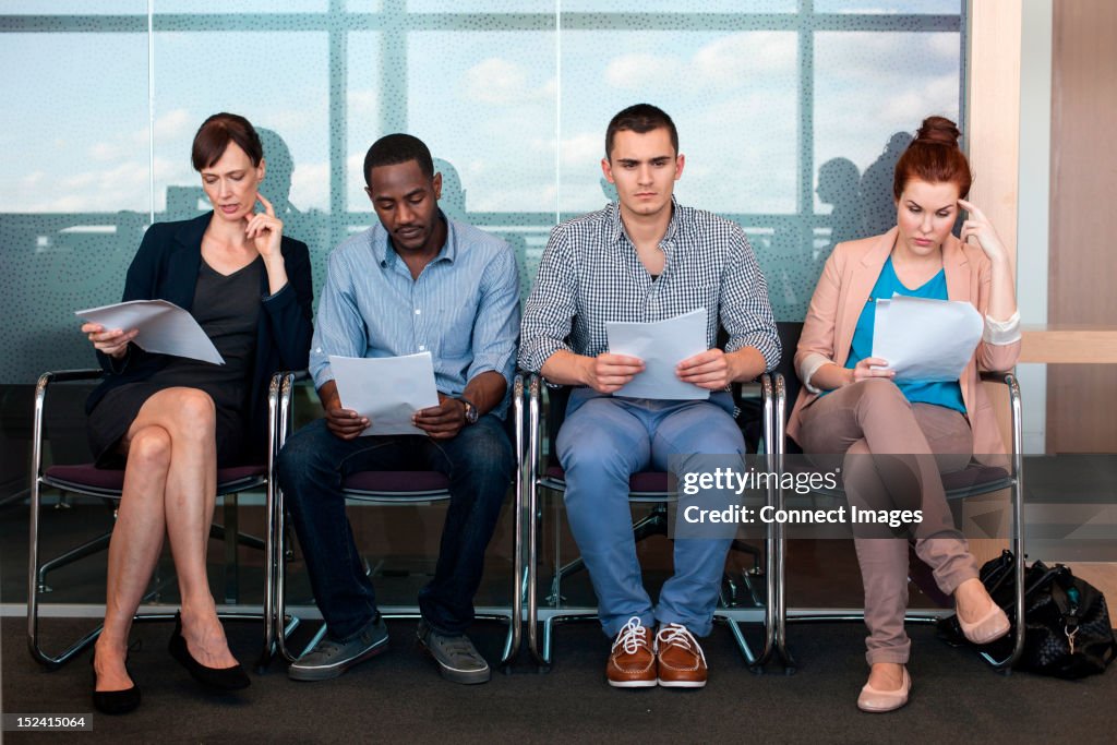 Four people sitting on chairs with documents