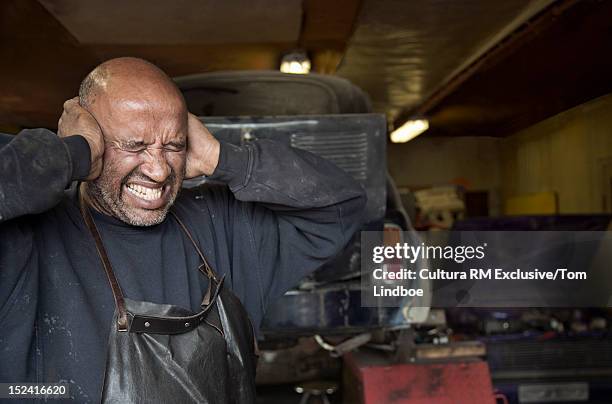 mechanic covering his ears in garage - ohrenschmerzen stock-fotos und bilder