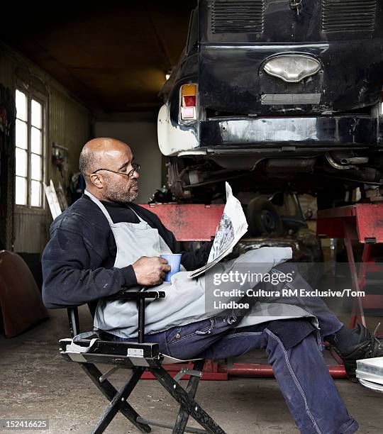 mechanic reading newspaper in garage - auto mechaniker stock-fotos und bilder
