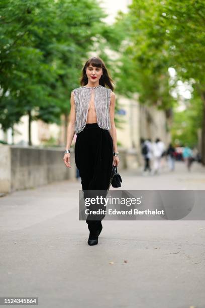 Mary Leest wears diamonds earrings, a rhinestones fringed open tank-top, black large velvet puffy pants, silver large bracelet, a black puffy velvet...