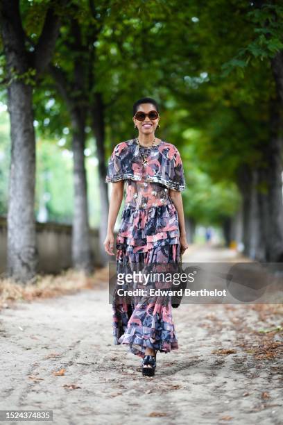 Tamu McPherson wears brown large circle sunglasses, black and gold handbag pendant earrings from Chanel, a navy blue / red / silver print pattern bat...