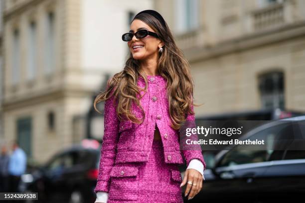Camila Coelho wears a black velvet headband, black sunglasses, a pink tweed jacket from Chanel, a matching pink tweed short skirt from Chanel, a...