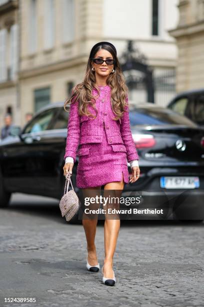 Camila Coelho wears a black velvet headband, black sunglasses, a pink tweed jacket from Chanel, a matching pink tweed short skirt from Chanel, a...