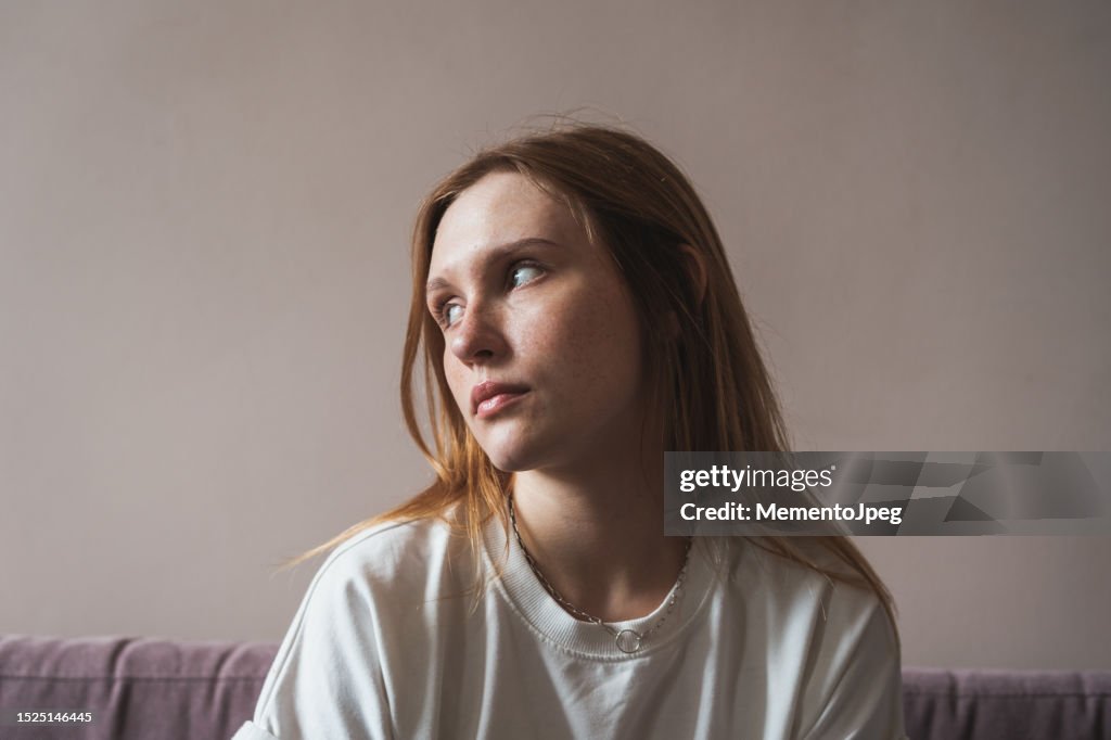 Teen depression. Portrait of sad upset redhead girl looking aside thinking about life problems, feeling lonely while spending time alone at home. Mental health, melancholy mood