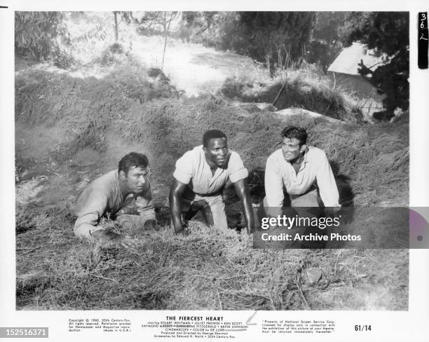 Ken Scott, Rafer Johnson, and Stuart Whitman crouching in ditch together in a scene from the film 'The Fiercest Heart', 1961.