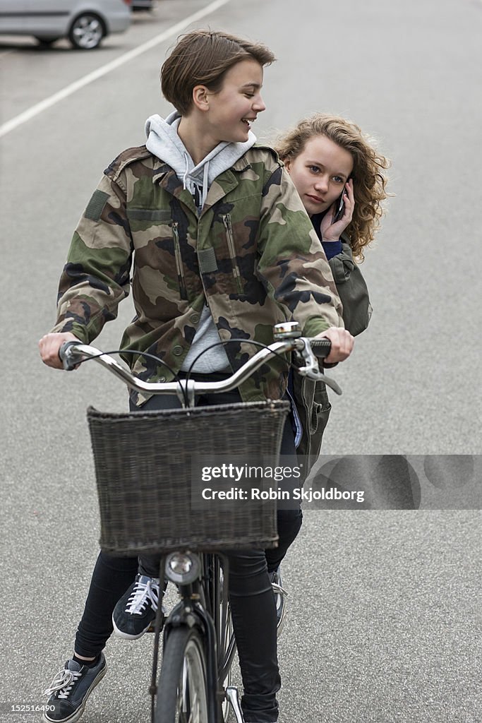 Two girls on bicycle, one girl with mobile