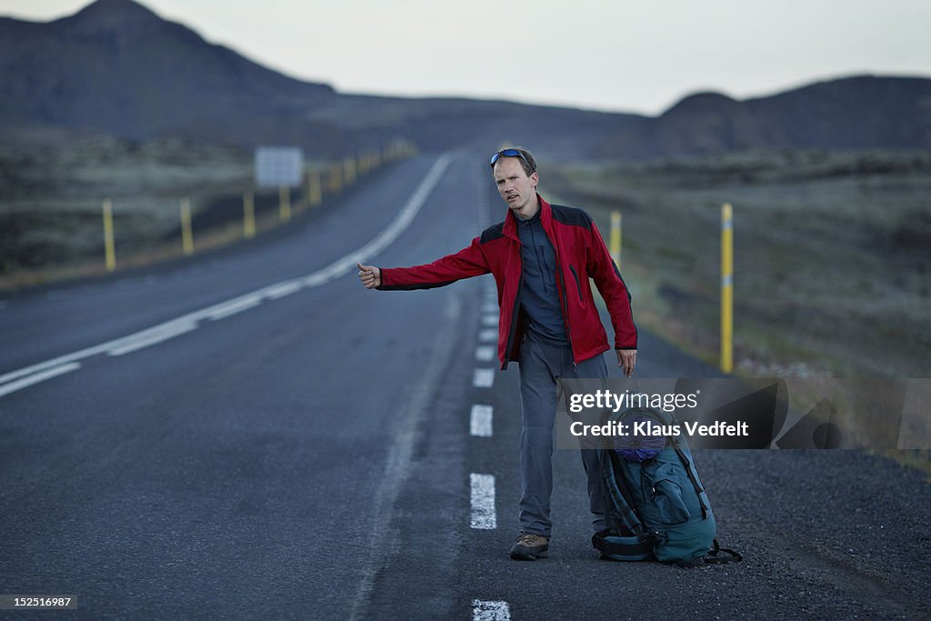 Male backpacker hitch hiking on long mountin road